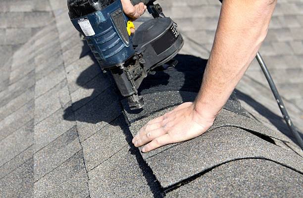 roof maintenance A roofer nails shingles over ridge vent material used on the peak of new residential house construction.